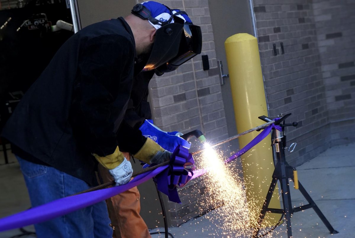 Senior Rian Fetting cutting the “ribbon” with a plasma arc cutter in front of the Welding Shop. 
