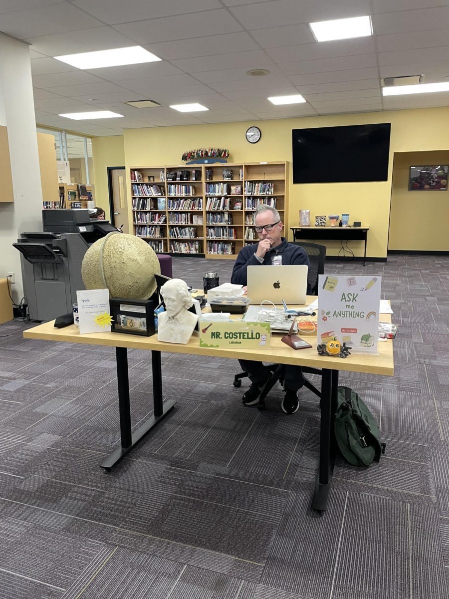 Mr. Costello waiting at his desk, ready to help readers find their next book.